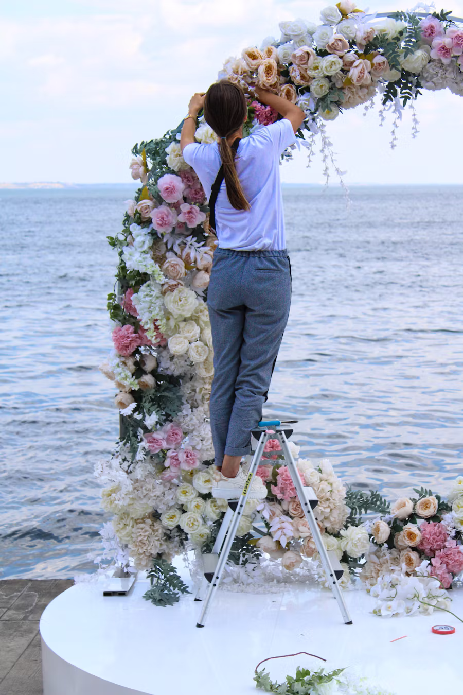 Installation d'une arche florale en cours, sur une échelle, en bord de mer